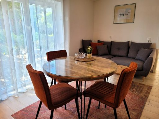 Modernes Wohnzimmer mit Essbereich, runder Tisch und gemütlicher Couch. Helle Vorhänge.